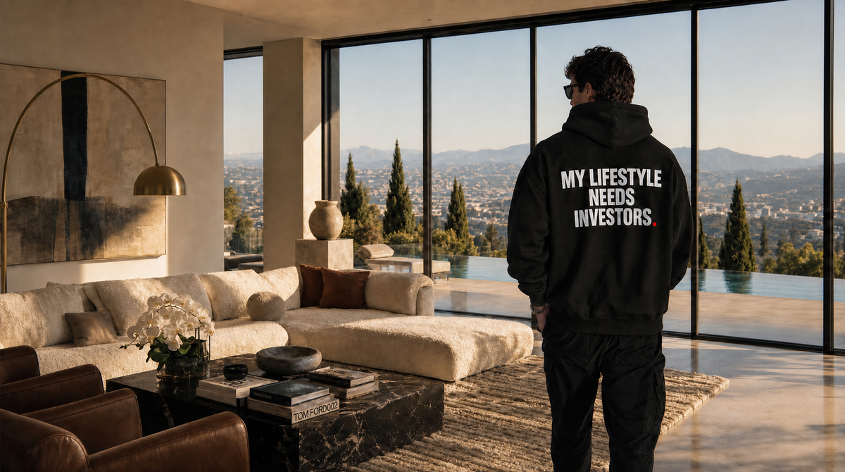 OVRSAID hoodie hero — male model from behind in a black oversized hoodie with MY LIFESTYLE NEEDS INVESTORS back print, modern villa living room